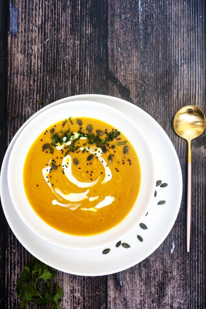 Sweet Potato Apple Carrot Soup in white plate on brown background