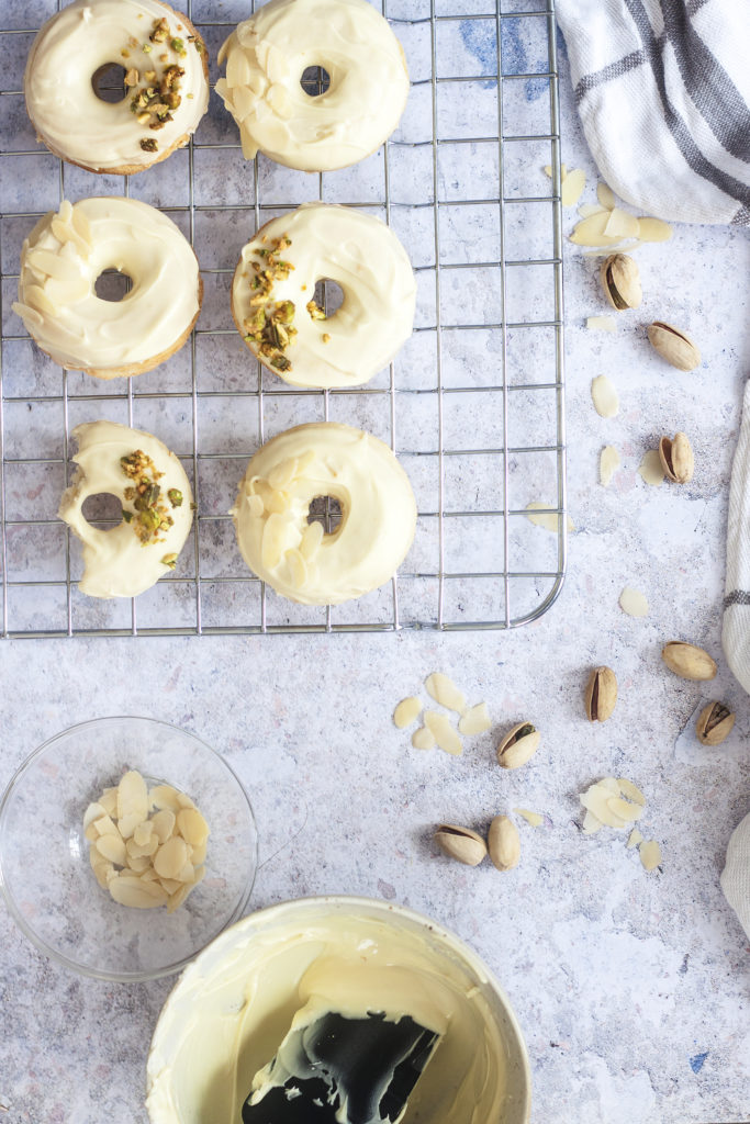 White Chocolate Ricotta Donuts on a wire rack and topped with crushed pistachios and almonds.