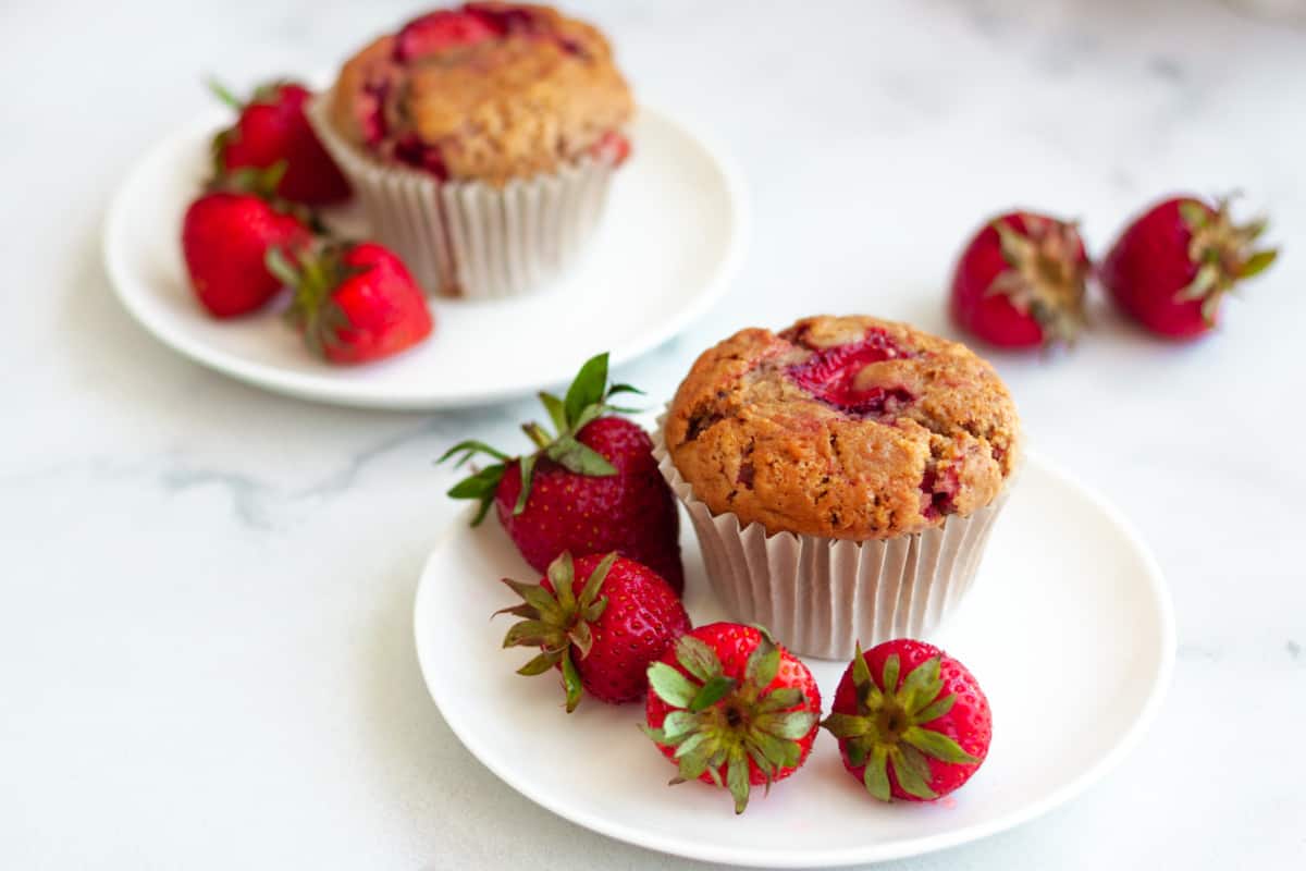 vegan strawberry muffins on a dessert plate surrounded by fresh strawberries