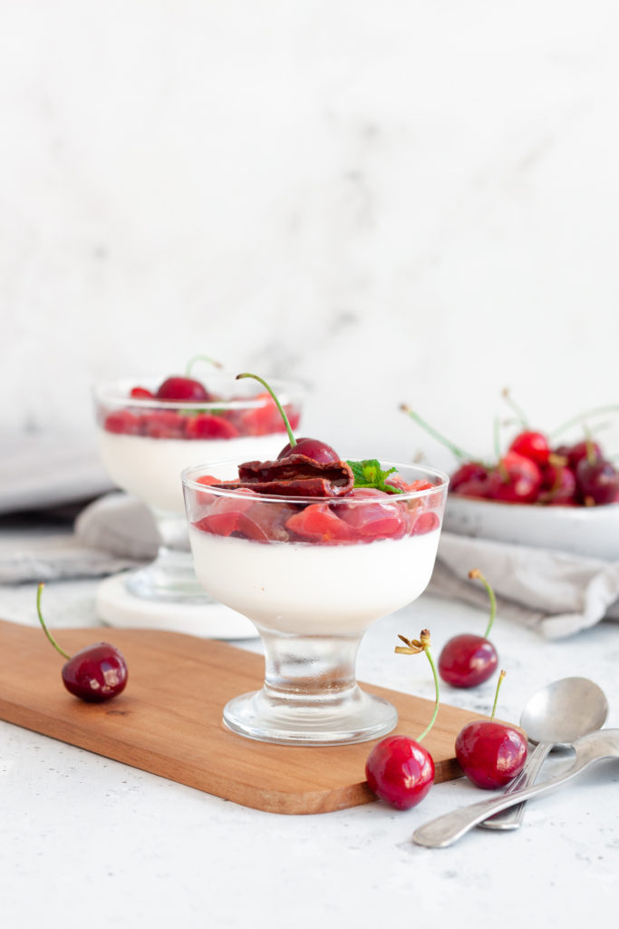 vertical image of 2 cherry panna cotta surrounded by fresh cherries