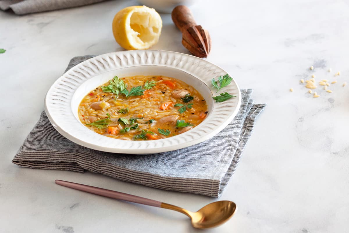 a plate of Vegan Orzo Soup on striped linen and a white background