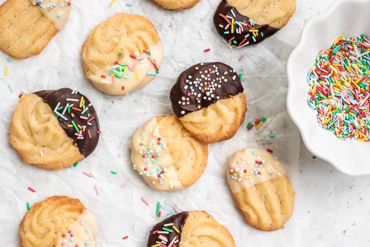 Italian Butter Cookies on parchment paper with a bowl of sprinkles