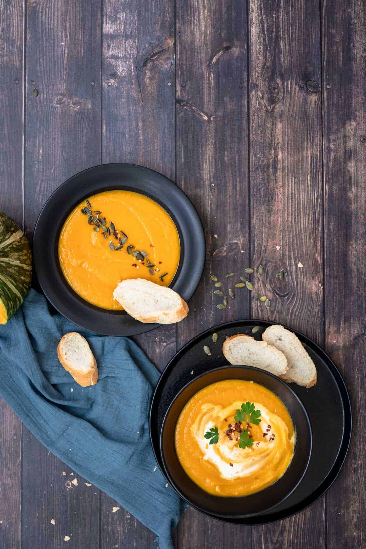 two servings of pumpkin carrot soup with slices of bread in a black soup plate.