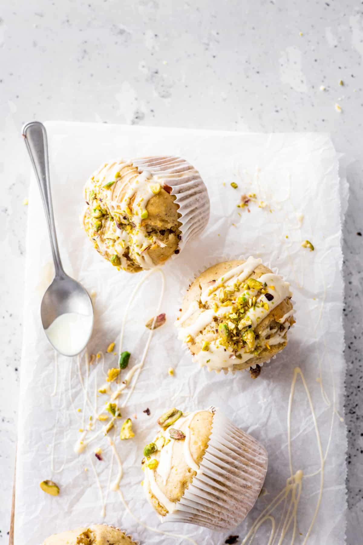 3 pistachio muffins with white chocolate glaze on a white background