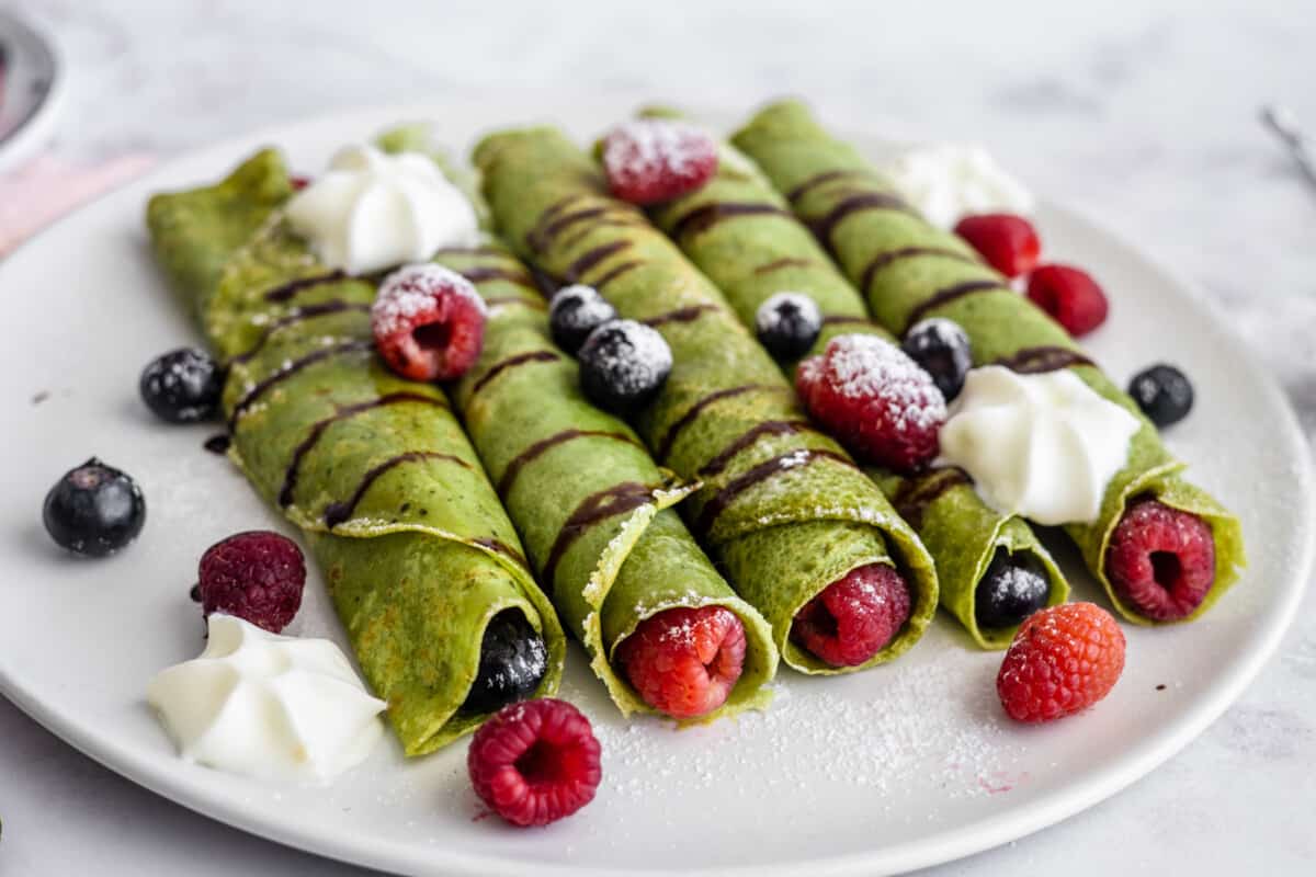 Five matcha crepes on a serving plate with fresh raspberries and blueberries.