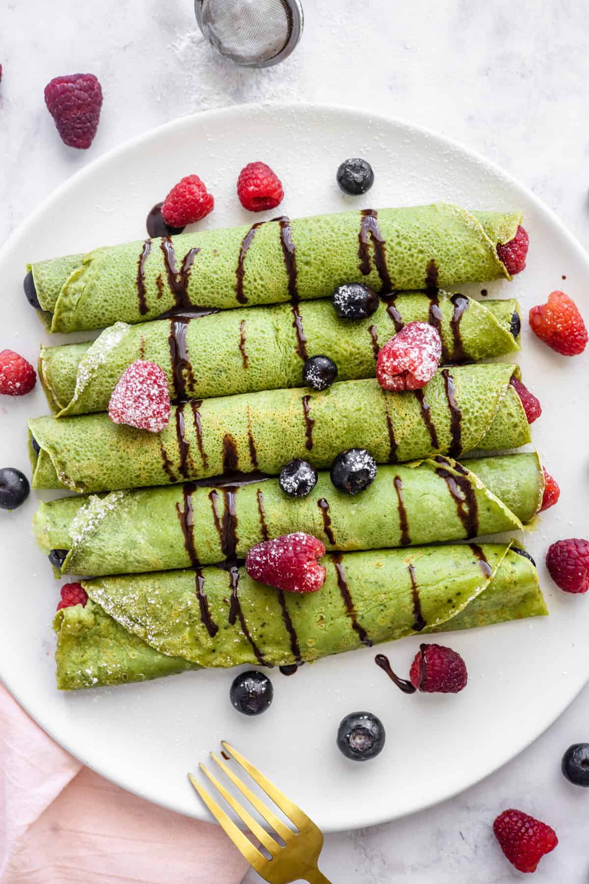 Five matcha crepes on a serving plate with fresh raspberries and blueberries.