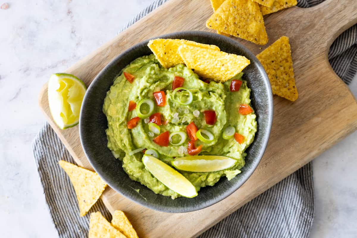 Guacamole in a large bowl, topped with chopped tomatoes and lime wedges.