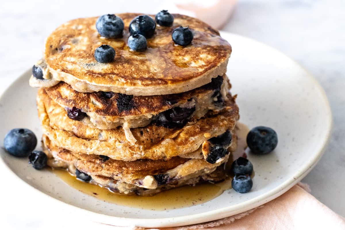 A stack of blueberry oatmeal pancakes with maple syrup.