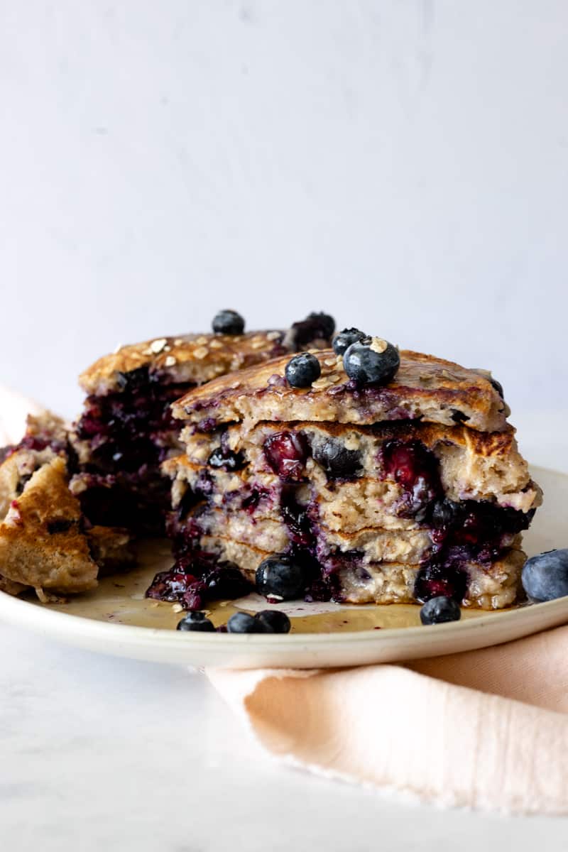 A stack of sliced oatmeal blueberry pancakes with maple syrup.